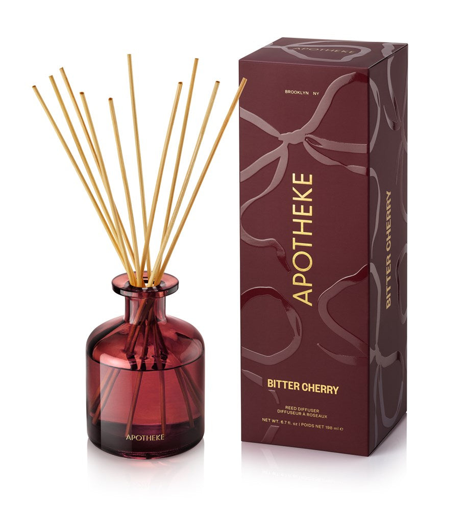 Apotheke Bitter Cherry diffuser with red bottle and wooden sticks next to its packaging on a white background