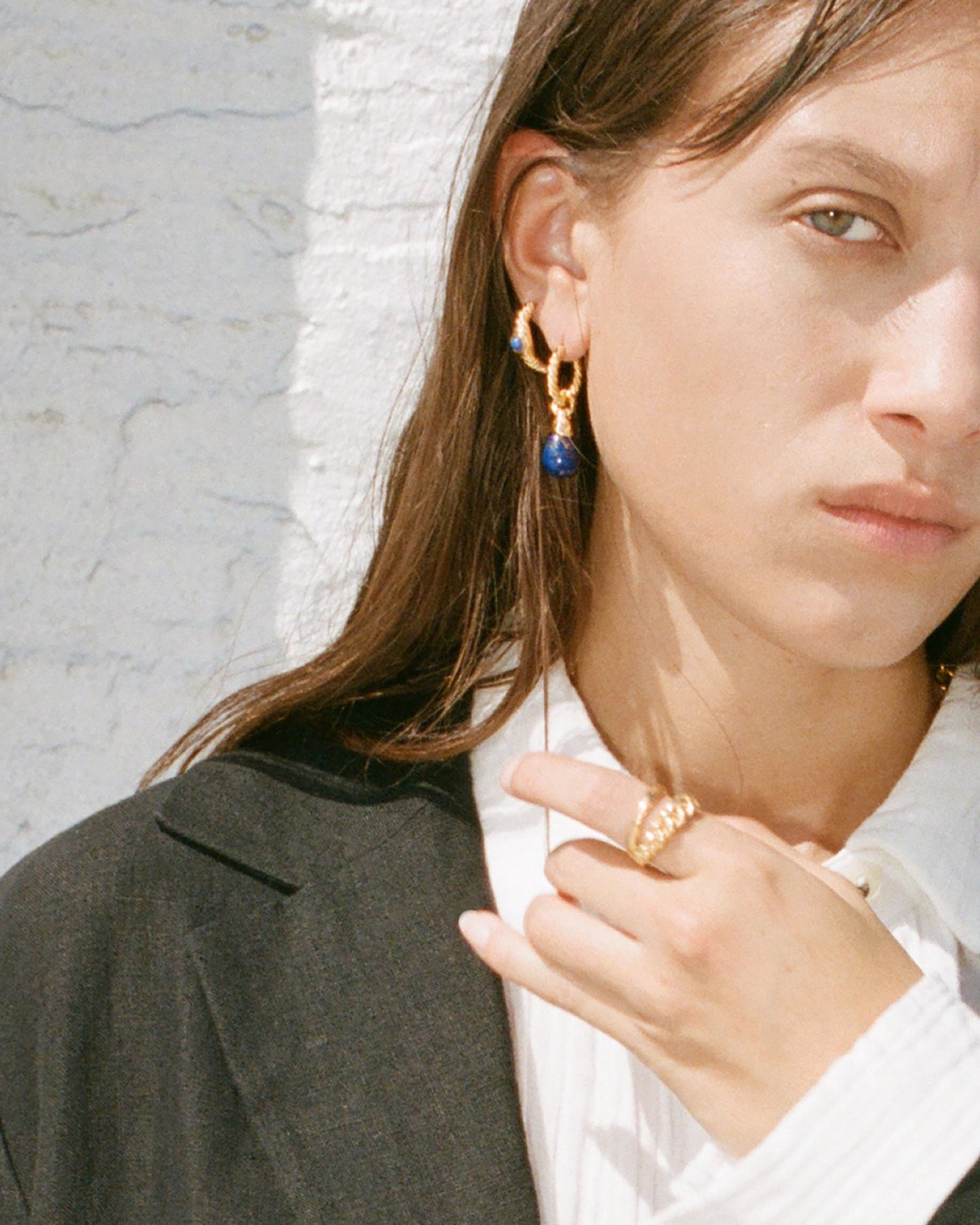 Woman wearing gold earrings and a ring against a light background