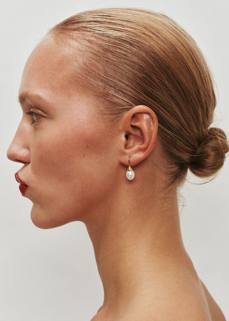Side profile of a woman with a bun and pearl earring on a plain background
