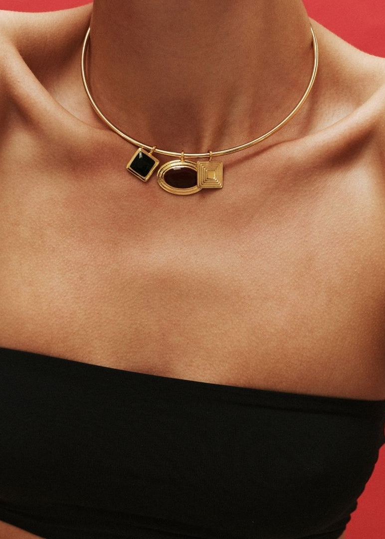 Gold necklace with black and gold pendants on a person against a red background