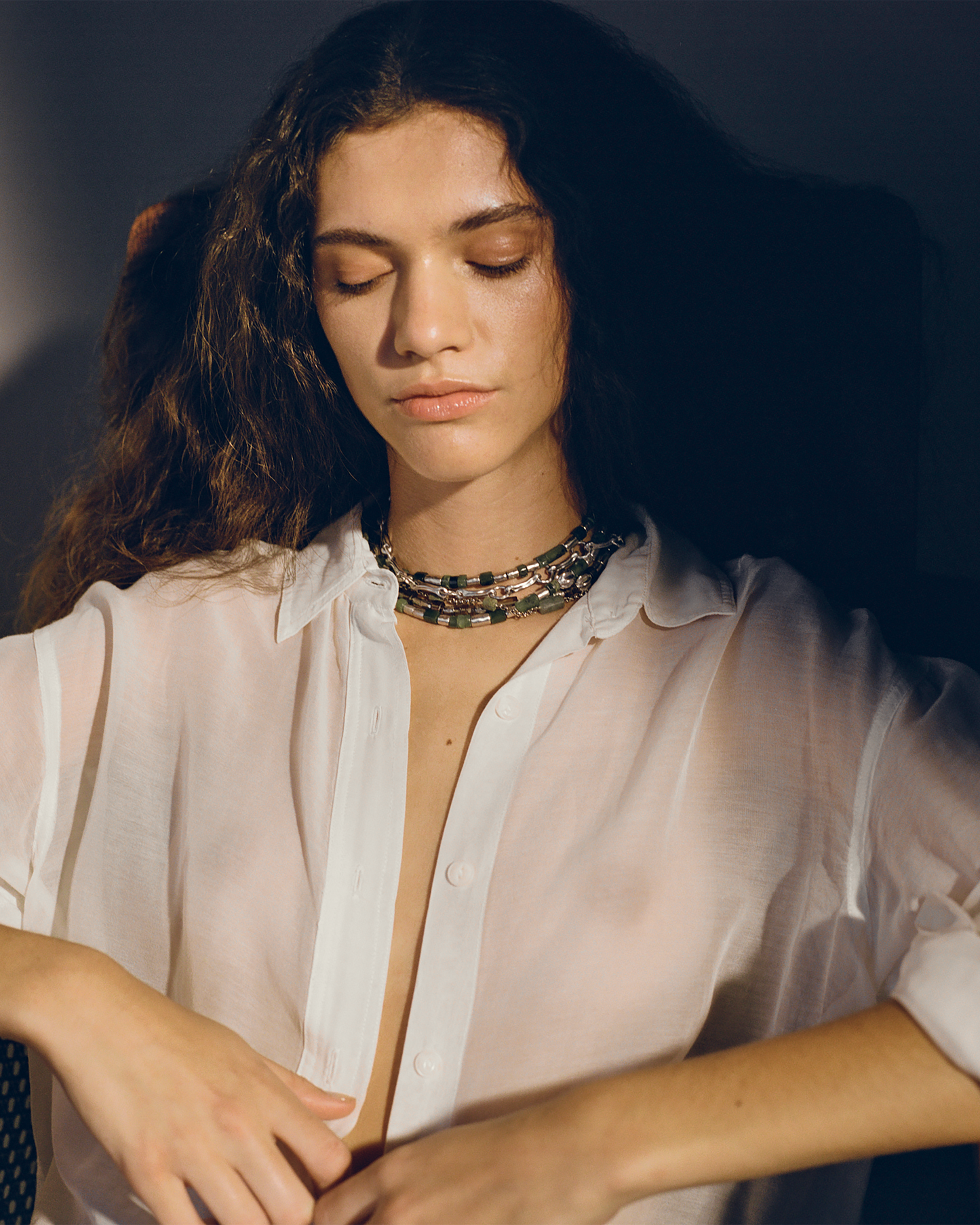 Woman wearing a light pink shirt and a patterned necklace against a dark background