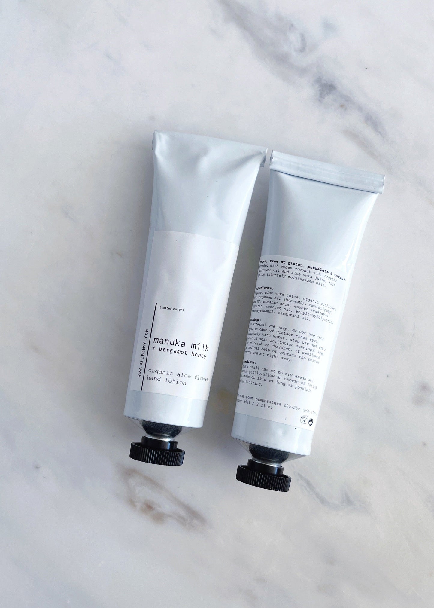 Two white hand cream tubes with black accents on a marble surface