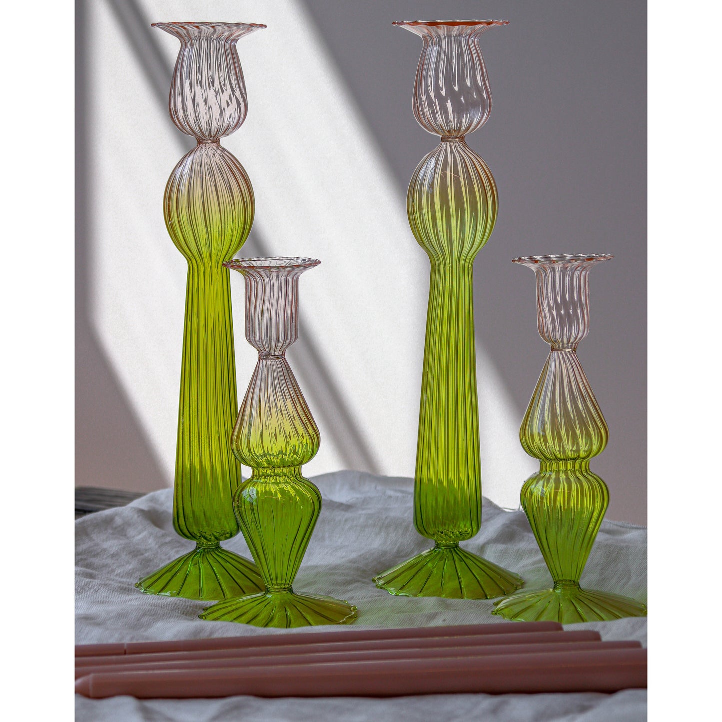 Set of green and pink glass candle holders on a white surface with a gray background