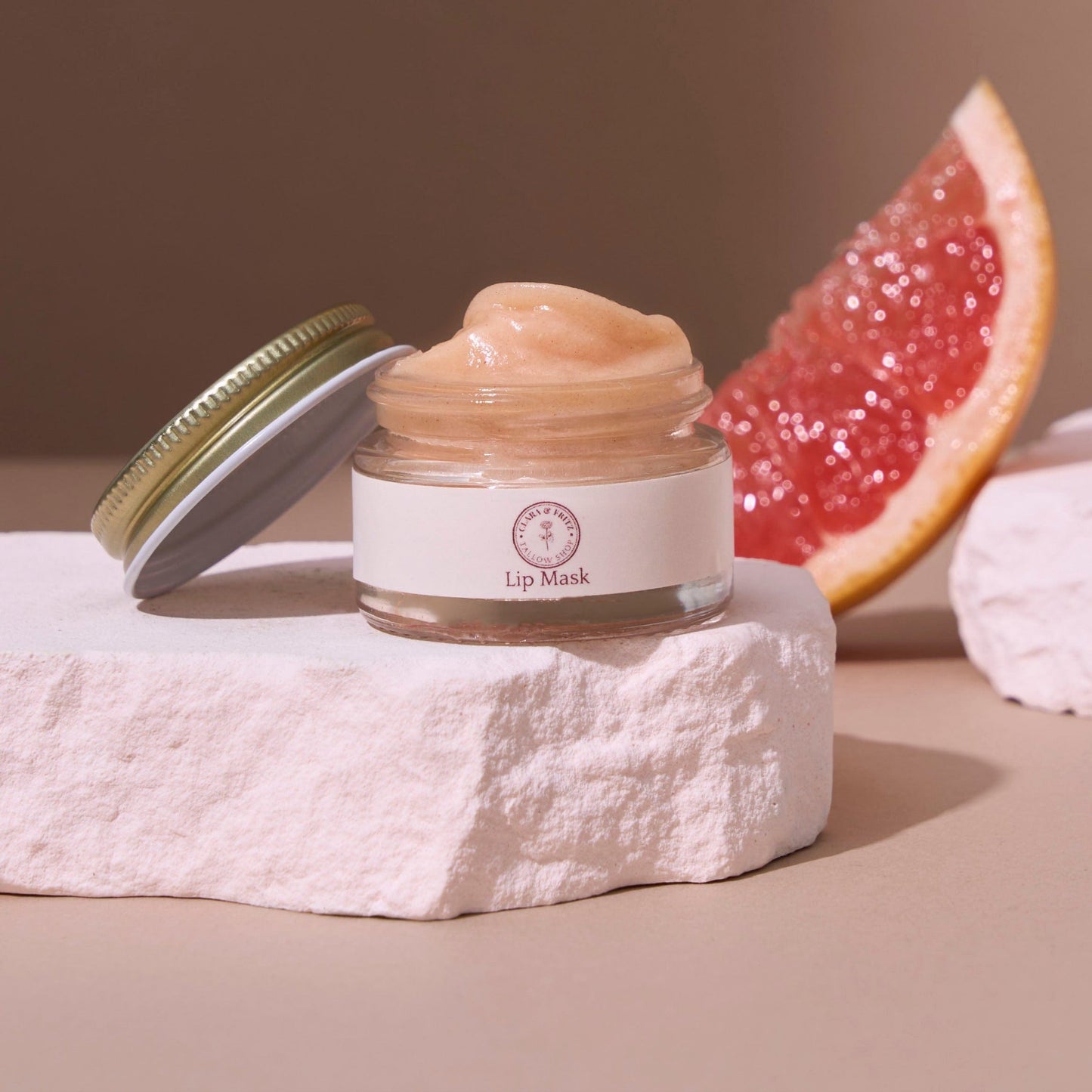 Jar of lip mask on a textured surface with a grapefruit half in the background