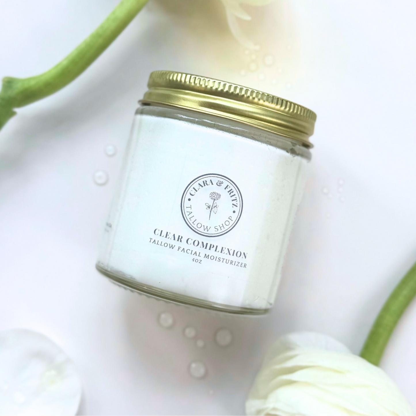 Jar of facial moisturizer with gold lid on a white background with green leaves.