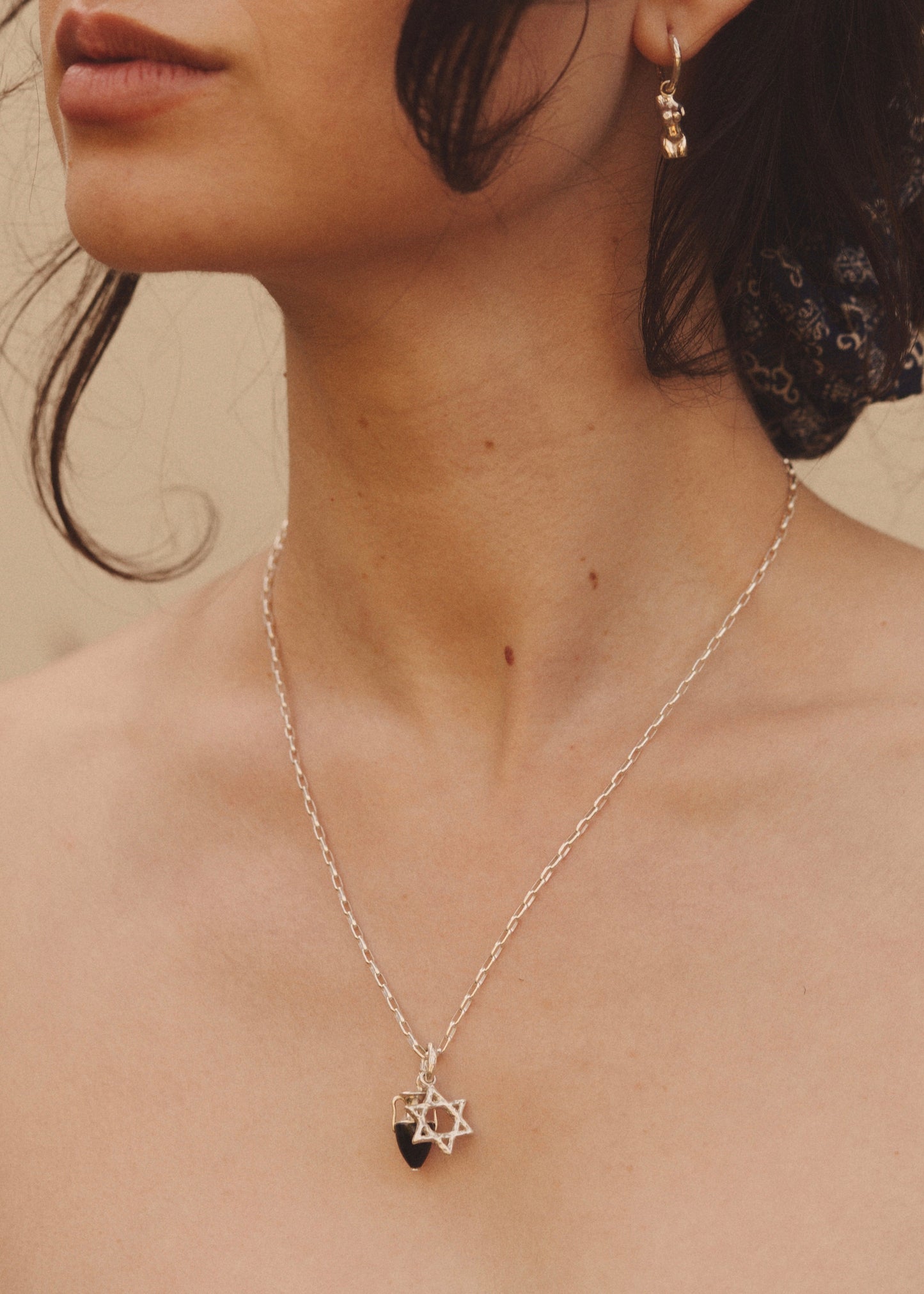 Woman wearing a silver necklace adorned with a silver star of David against a neutral background. 