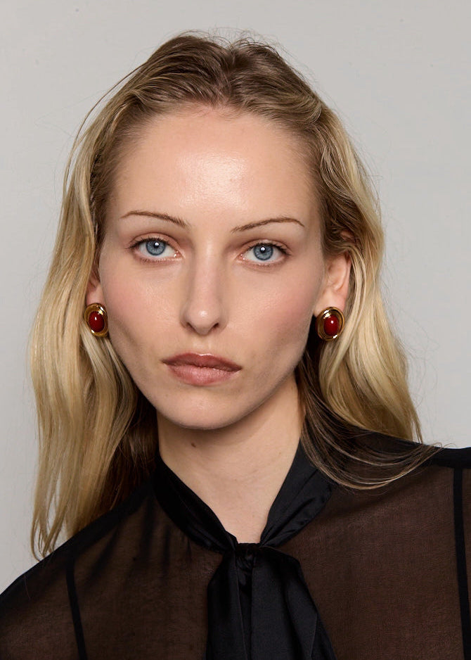 Woman with blonde hair wearing red earrings against a neutral background