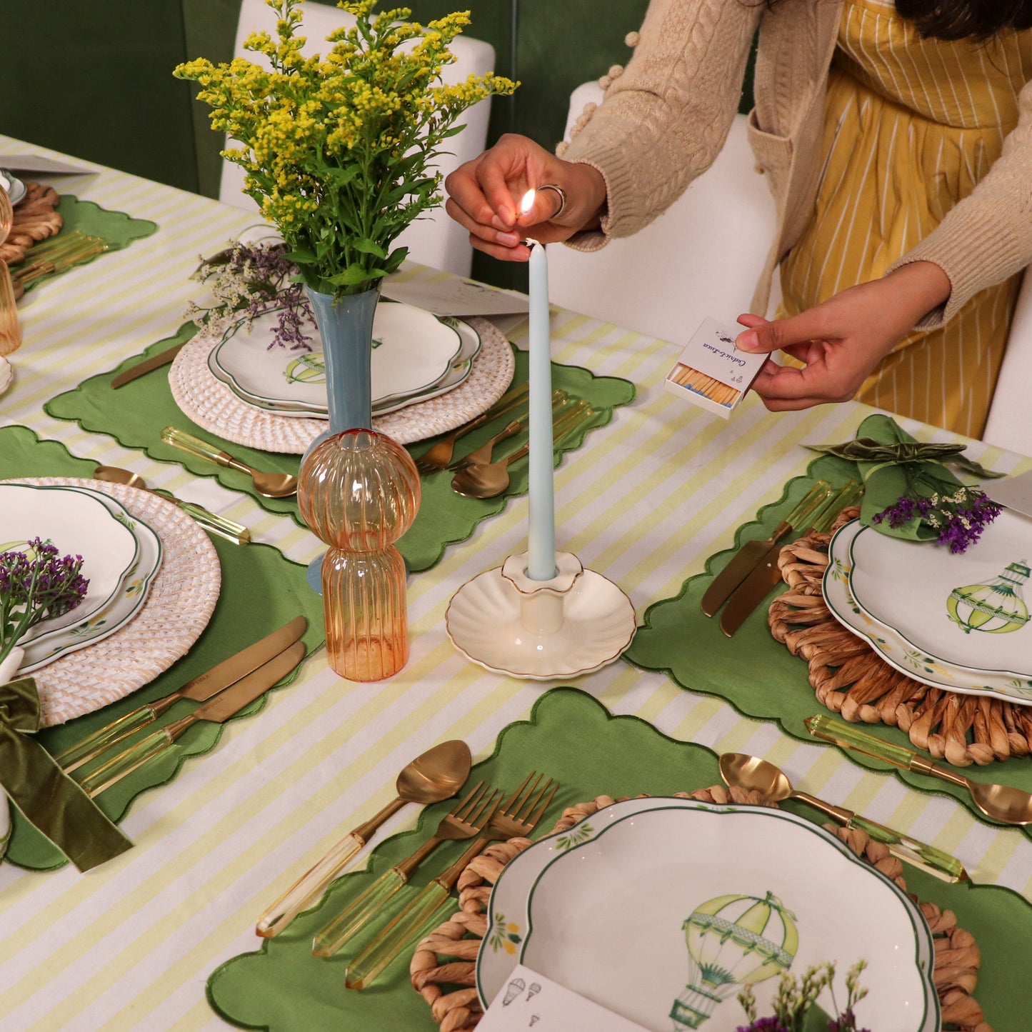 Table setting with plates, cutlery, and a candle being lit on a tablecloth.