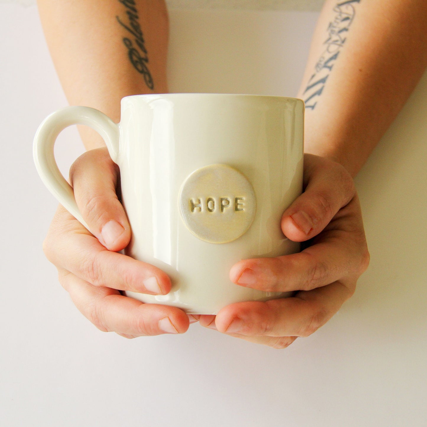 Person holding a white mug with 'HOPE' on a light background