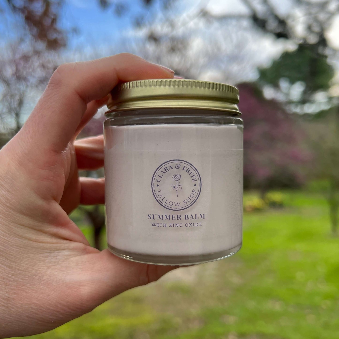 Hand holding a jar of 'Summer Balm' with a blurred outdoor background