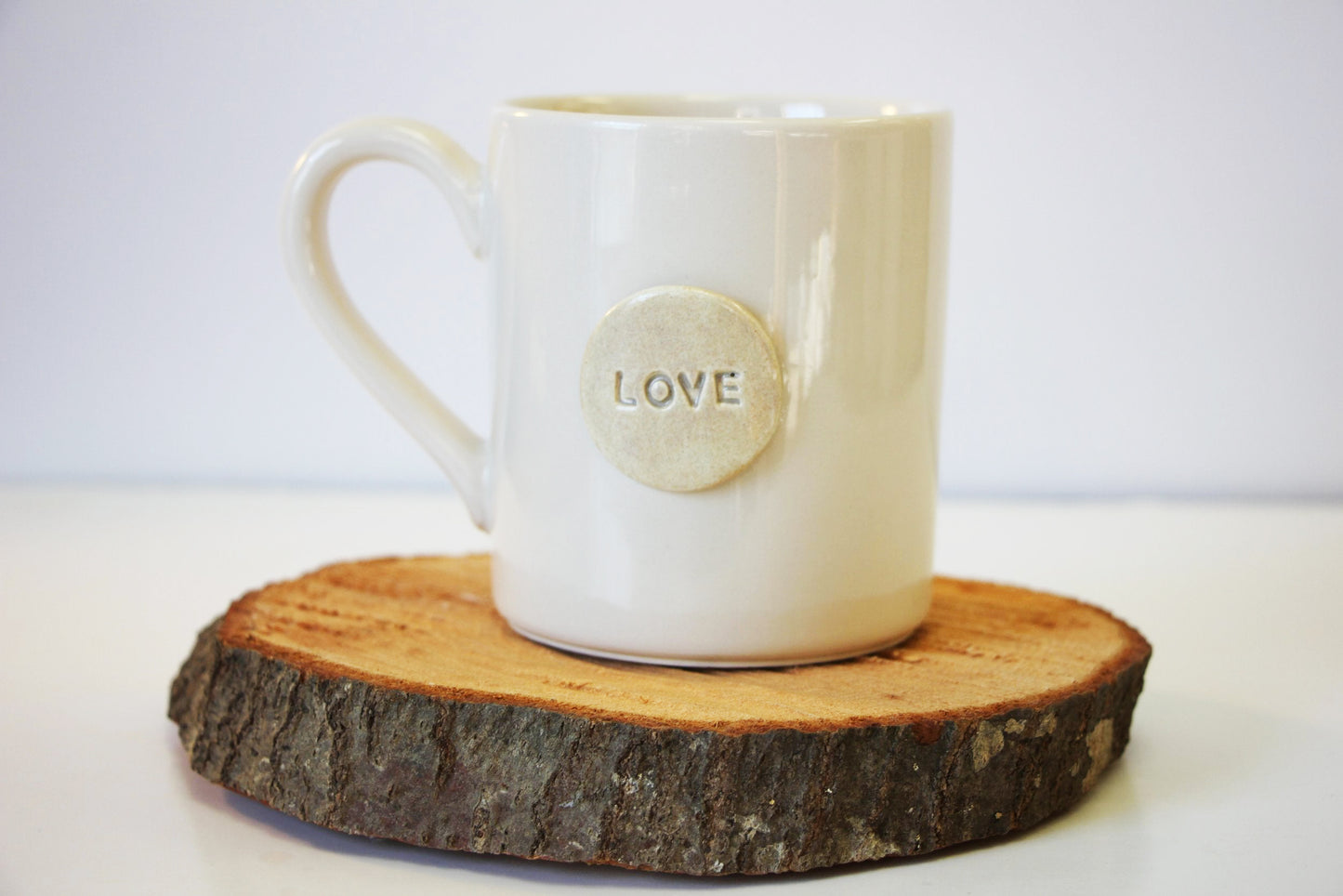 White mug with 'LOVE' on a wooden coaster against a white background