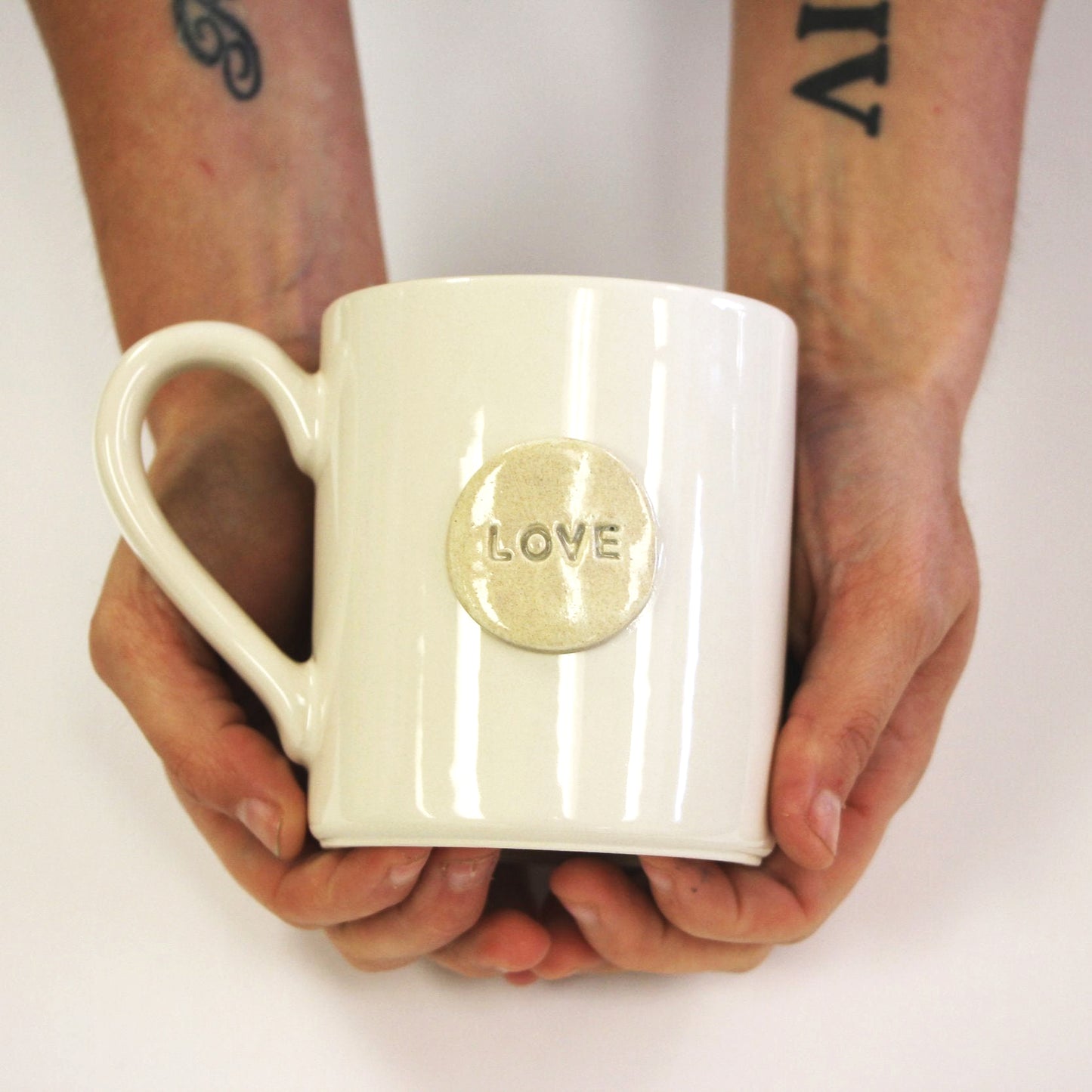 White mug with 'LOVE' emblem held by hands on a white background