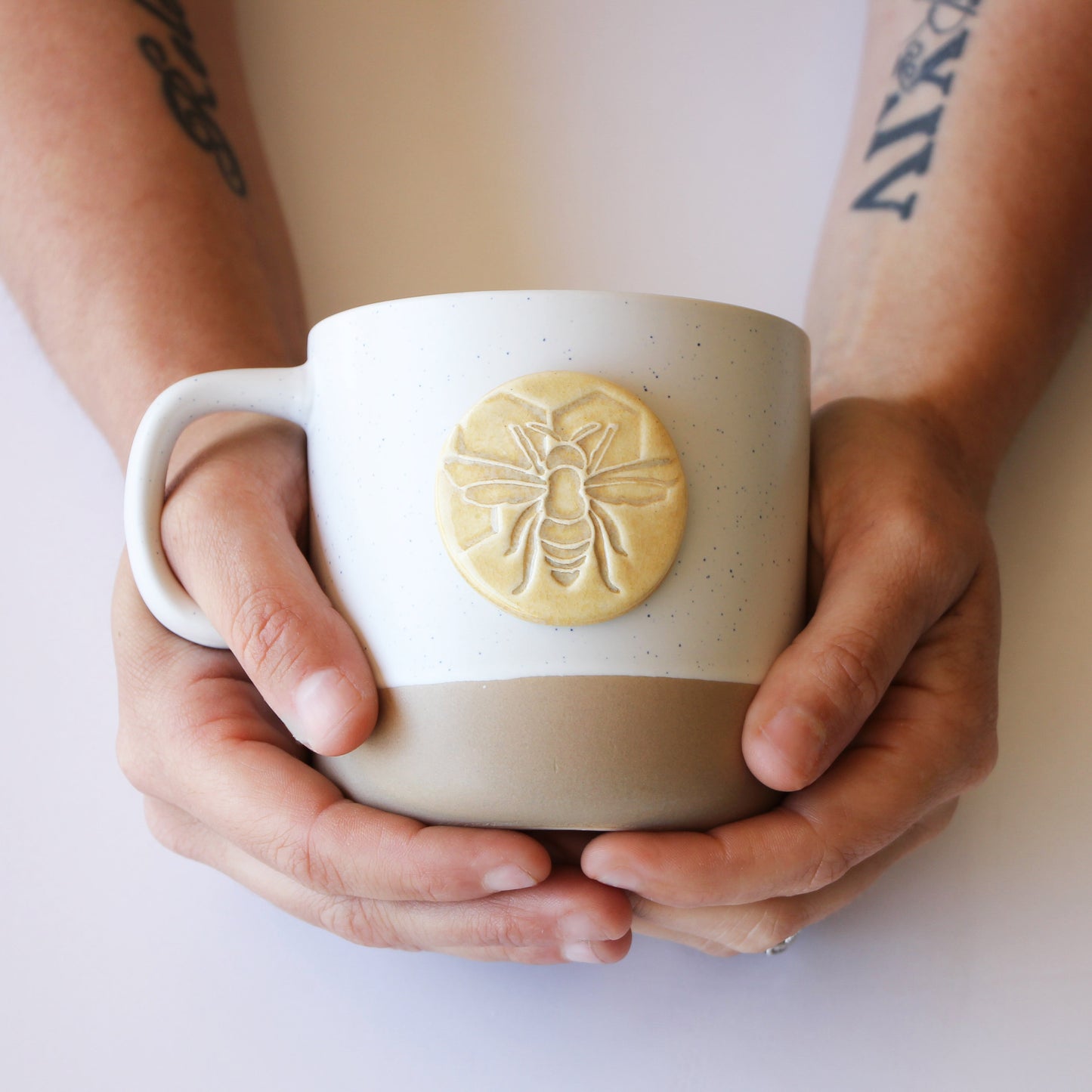 Person holding a ceramic mug with a bee design on a white background