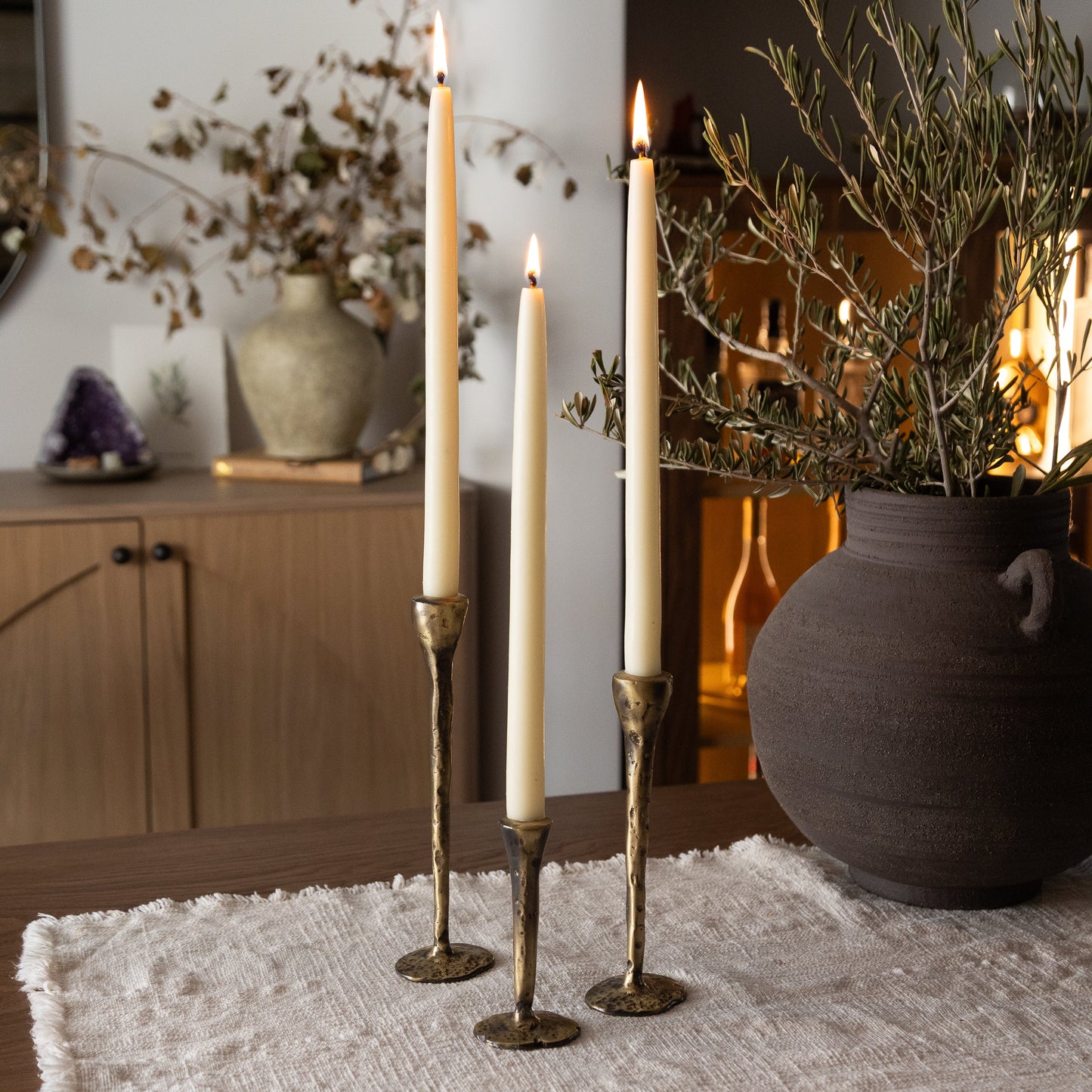 Three tall candles in gold candlesticks on a textured surface with decorative elements in the background.