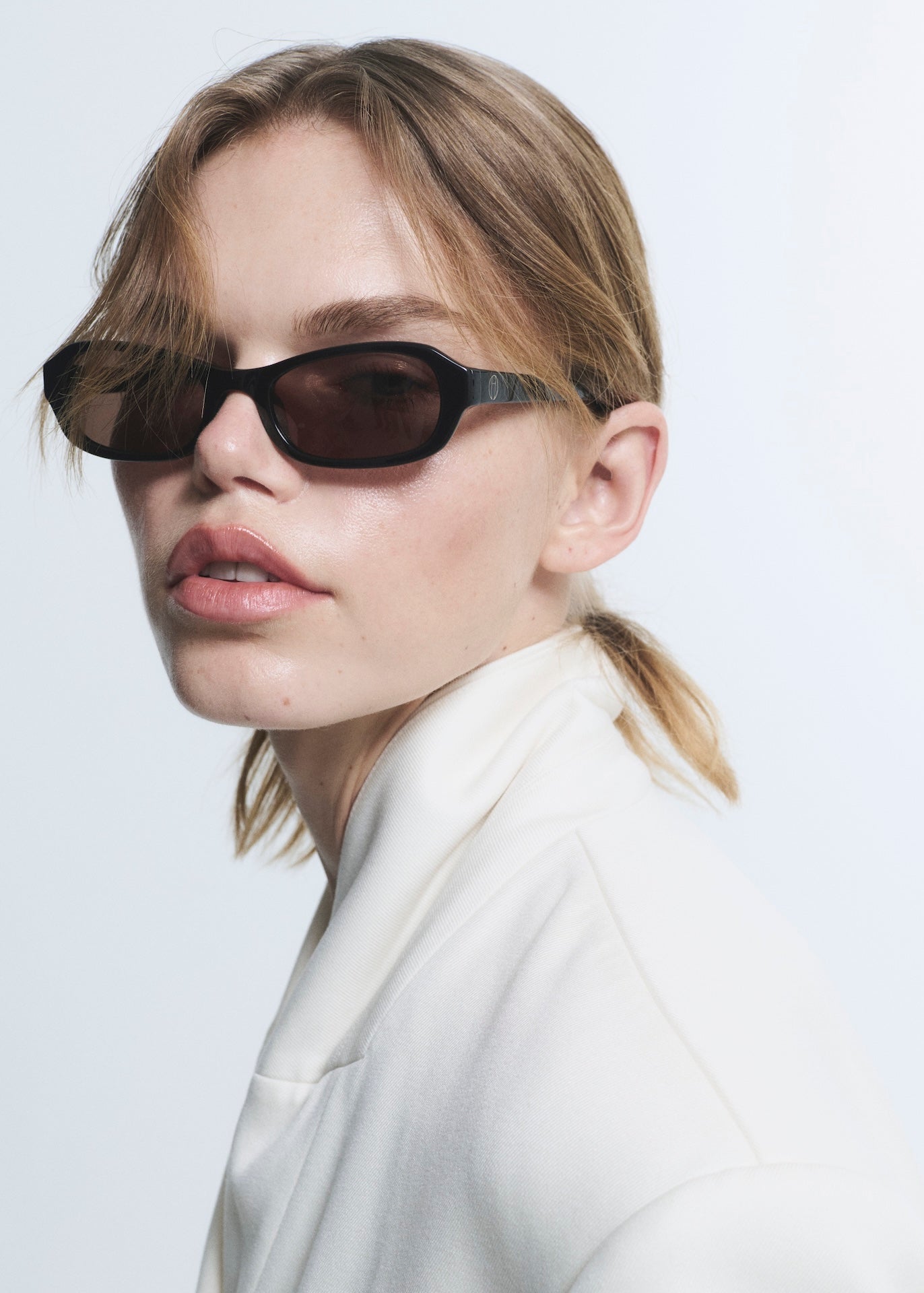 Person wearing black sunglasses and a white outfit on a light background