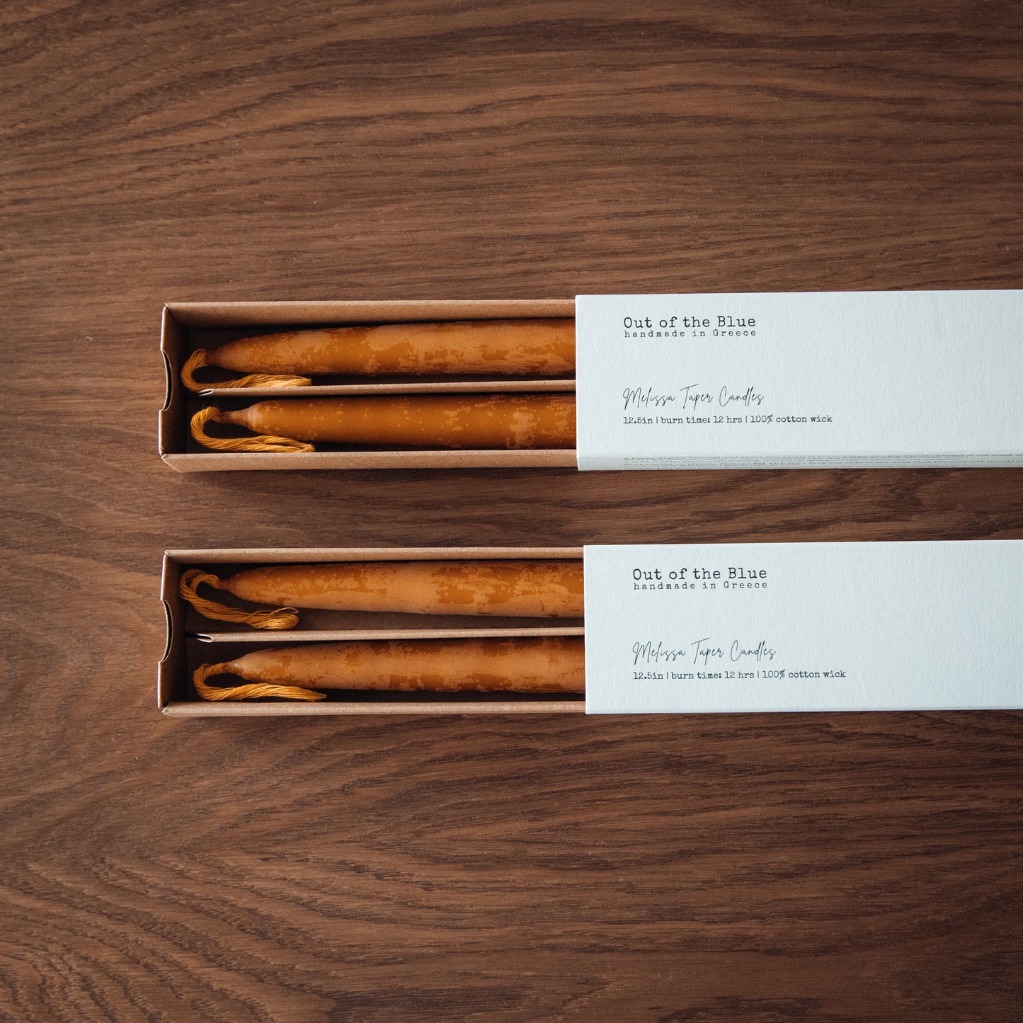 Two sets of candles in cardboard boxes on a wooden surface, with 'Out of the Blue' branding.