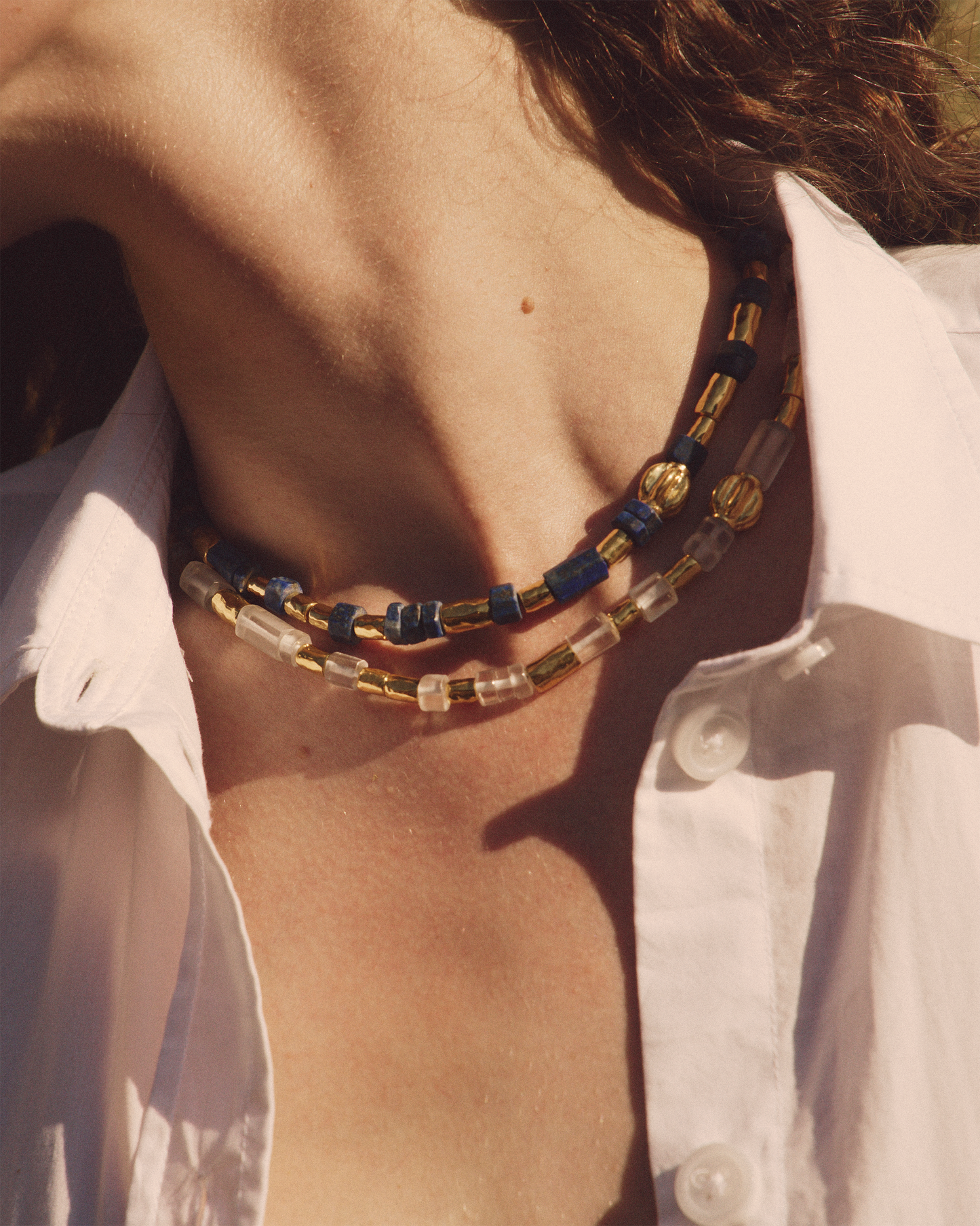 Close-up of a person wearing a necklace with blue and gold beads, with a blurred background.