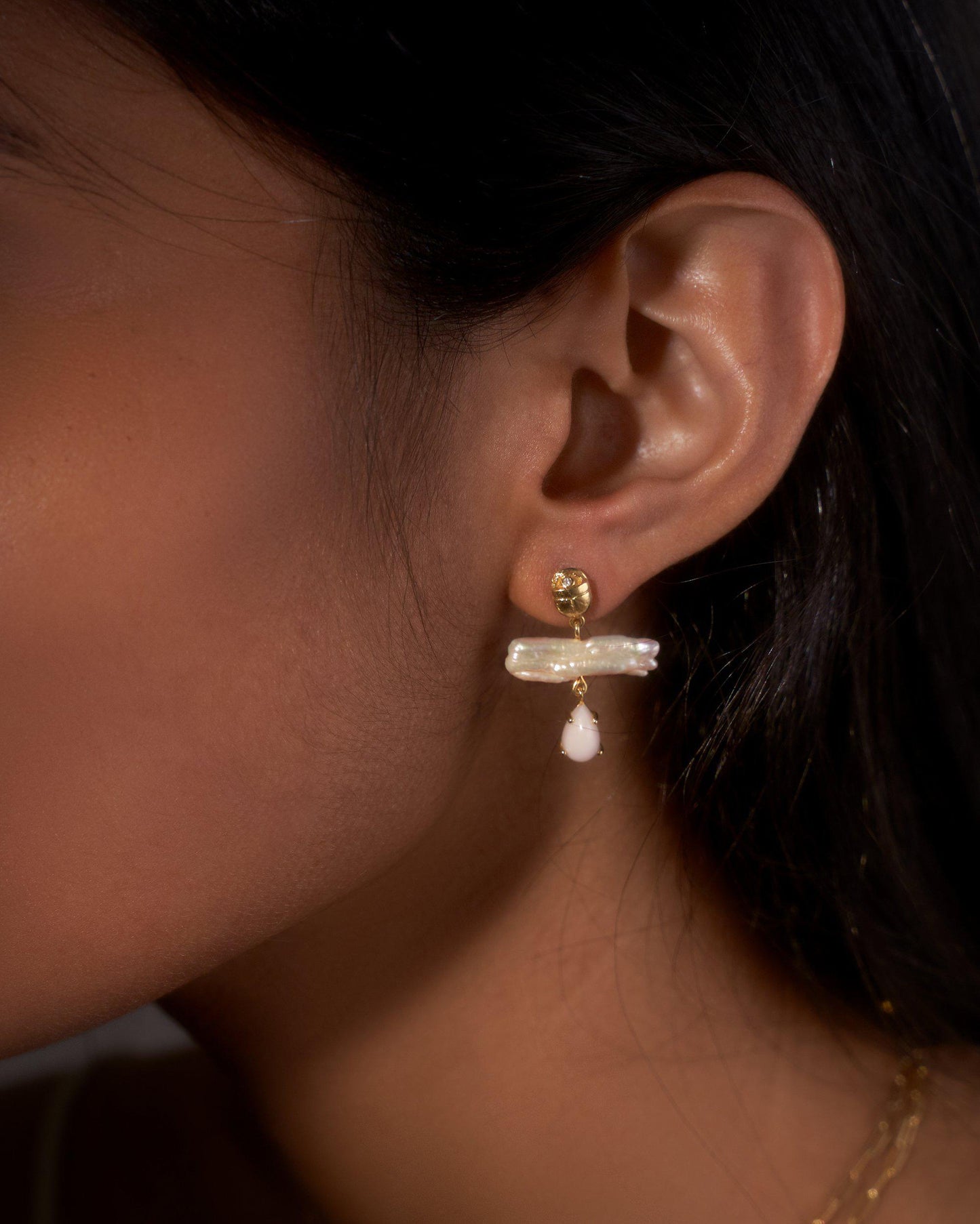 Close-up of an ear wearing a gold earring with a pearl drop.