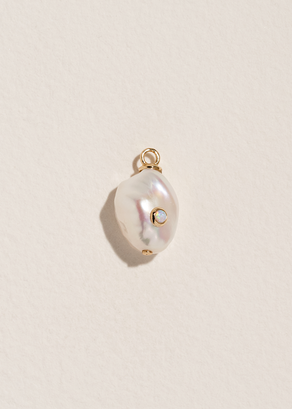 Baroque pearl pendant with gold and opal stone accents on a beige background