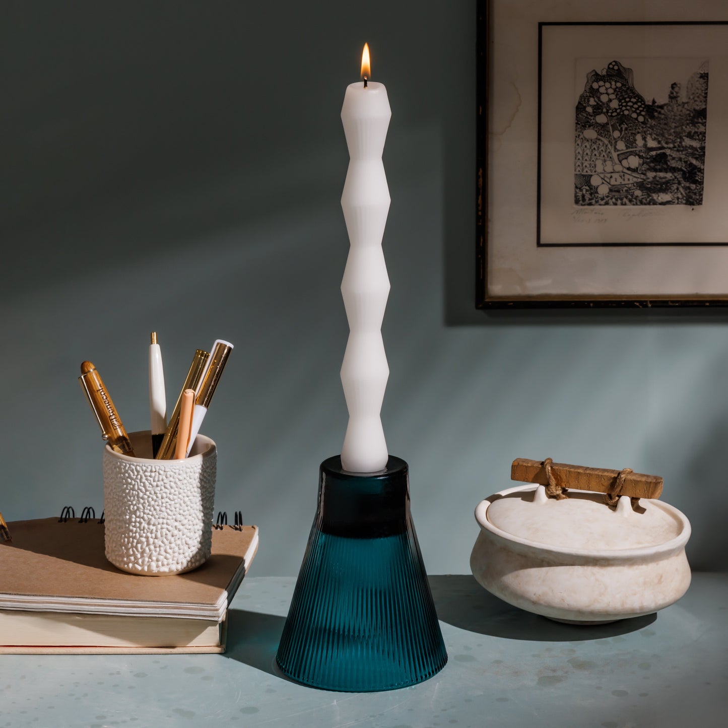 White candle in a blue holder on a surface with books and decorative items.
