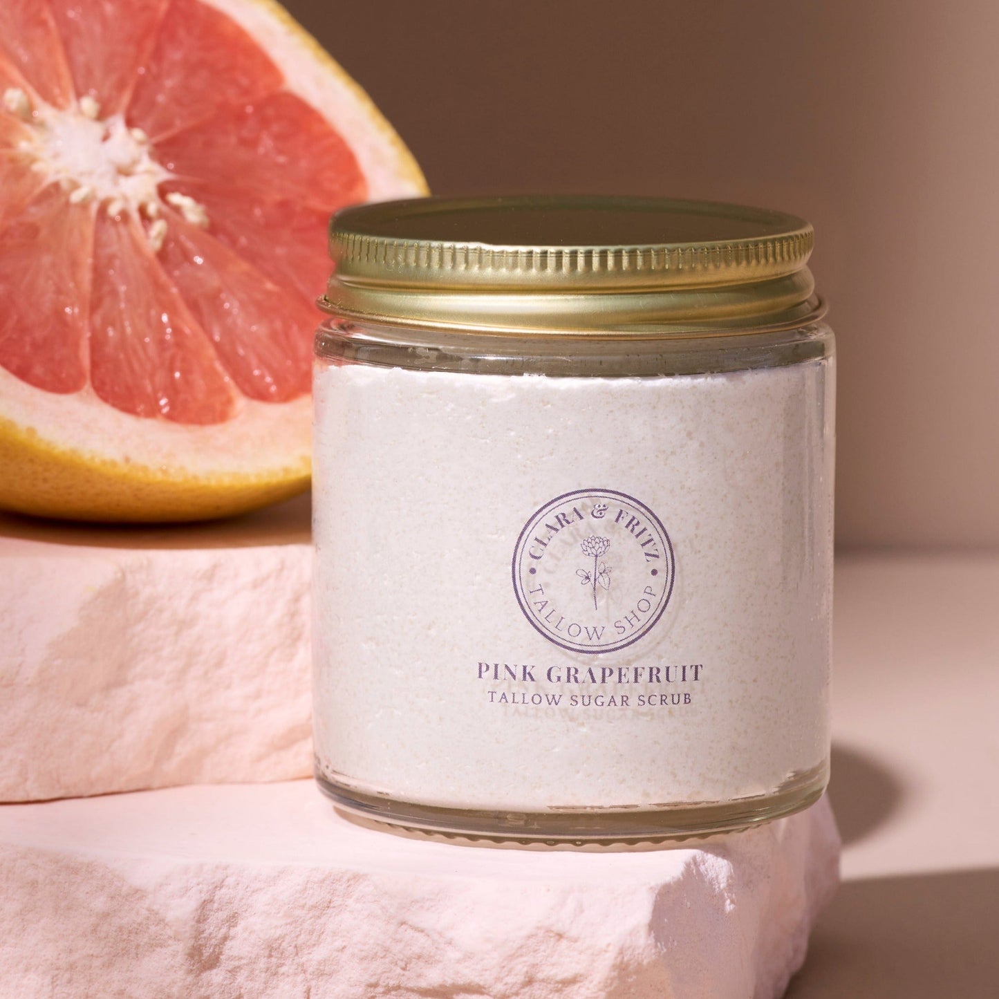Jar of pink grapefruit scrub with a sliced grapefruit on a neutral background