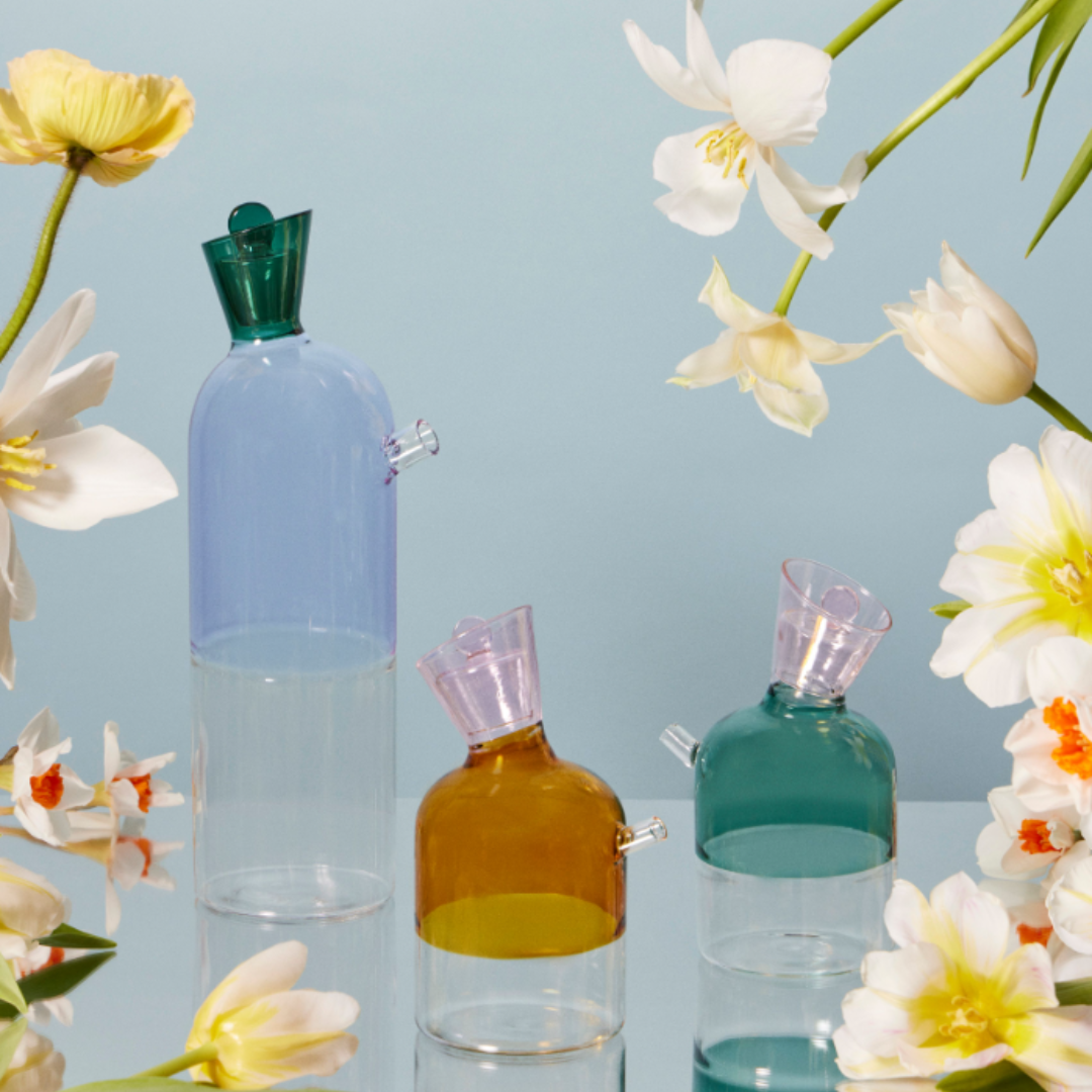 Set of glass bottles with colorful caps surrounded by flowers on a light blue background