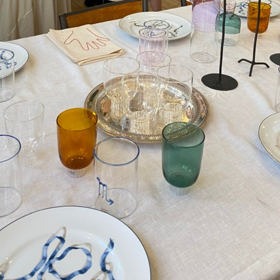 Dining table with colorful glasses, plates, and a silver tray on a white tablecloth.