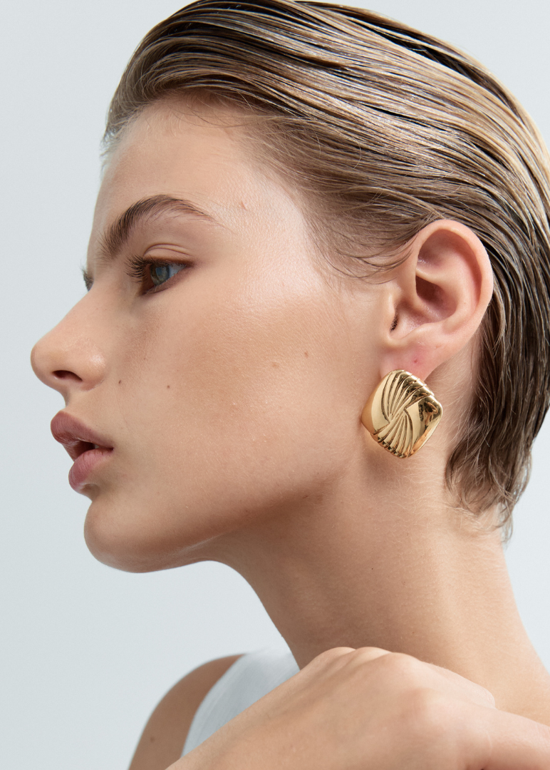 Woman wearing gold earrings against a light gray background