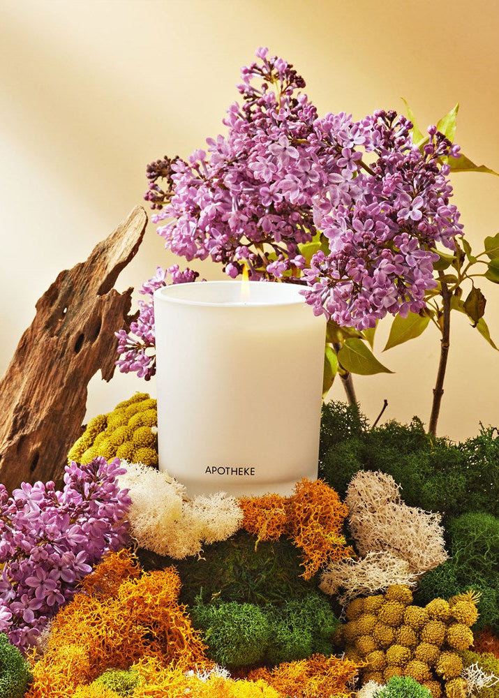 Candle with purple flowers and greenery on a neutral background