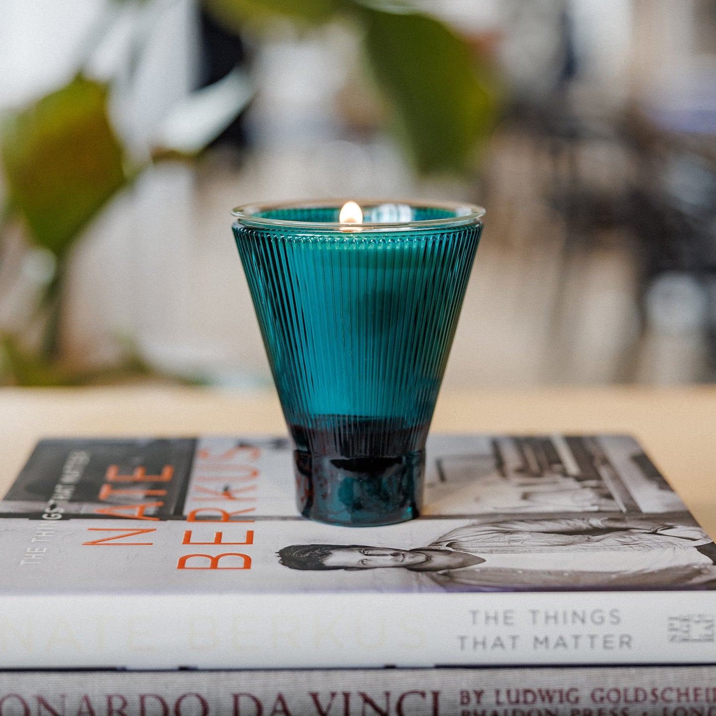 Blue candle in a textured glass holder on top of books with a blurred background