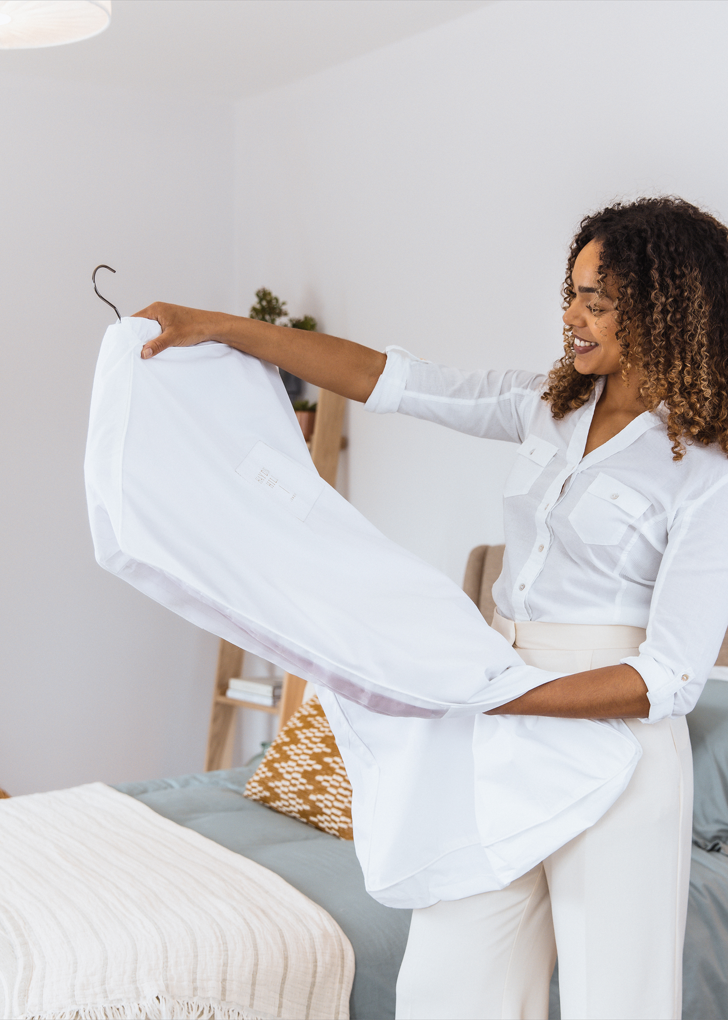 Woman holding a white cotton garment bag in a bedroom setting