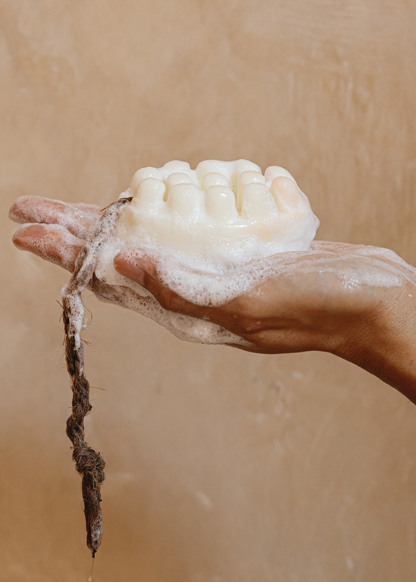 Hand holding a bar of Palo Santo soap with foam against a beige background. 