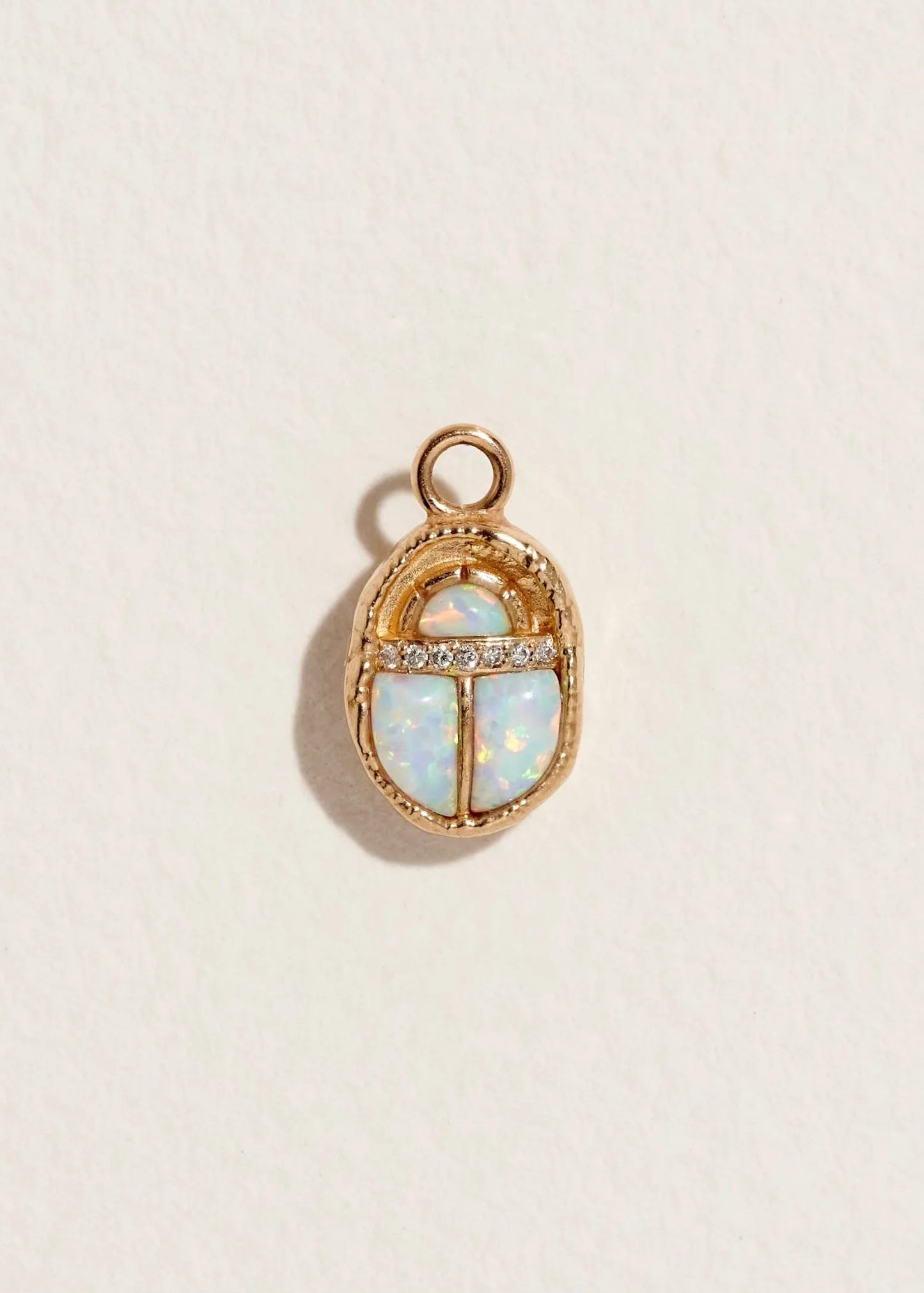 14K gold scarab pendant with pave diamonds and opal stone on a beige background