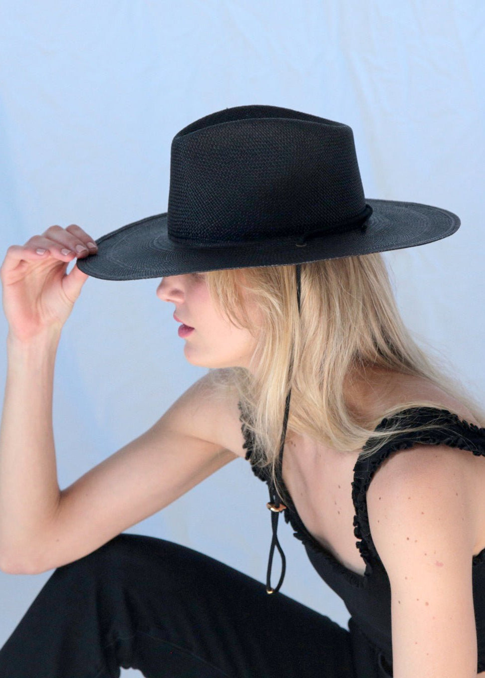 Woman wearing a black wide-brimmed hat against a light blue background