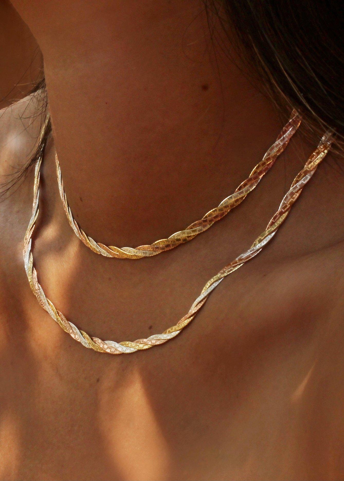Close-up of a person wearing two gold necklaces with a blurred background