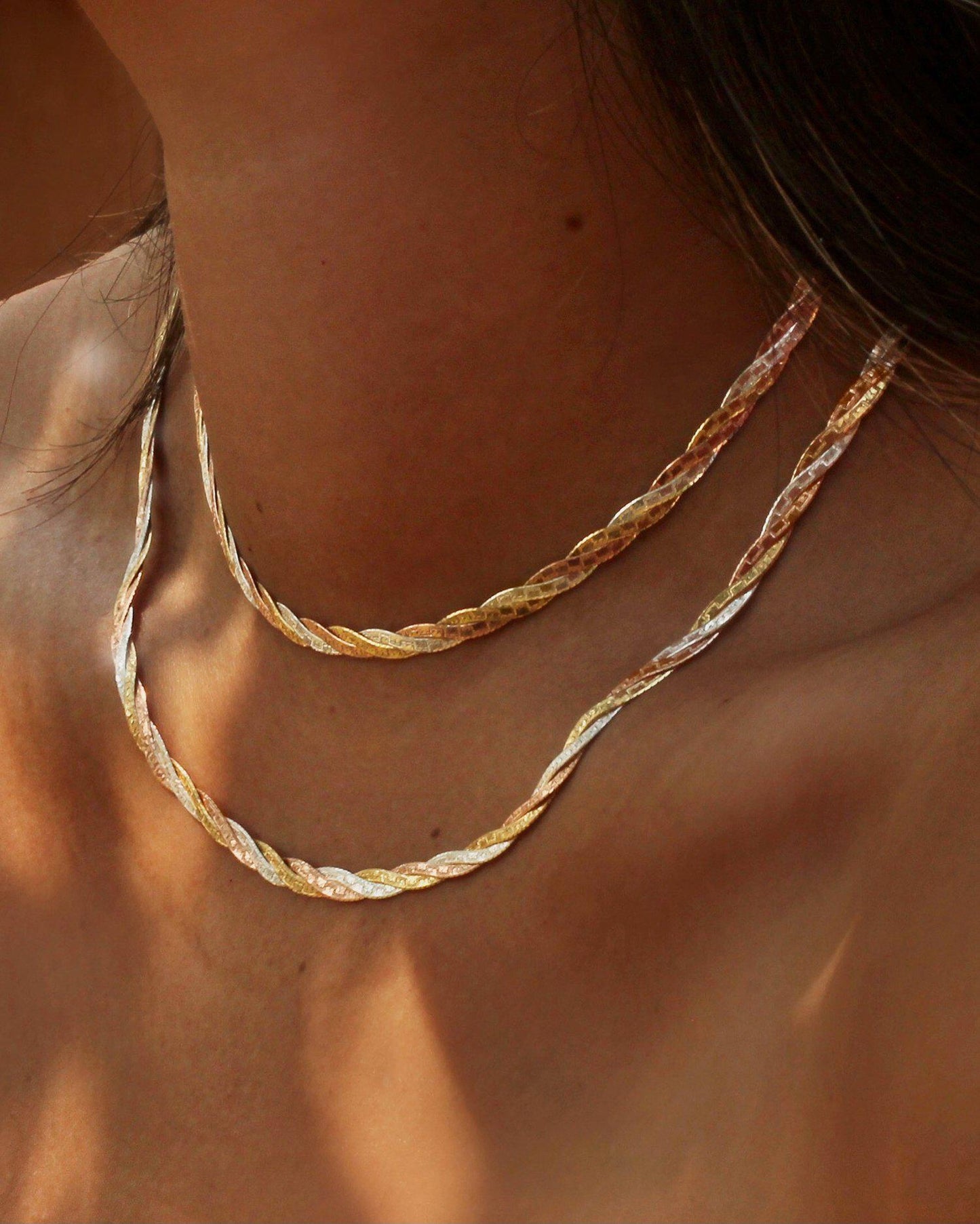 Close-up of a person wearing two gold necklaces with a blurred background